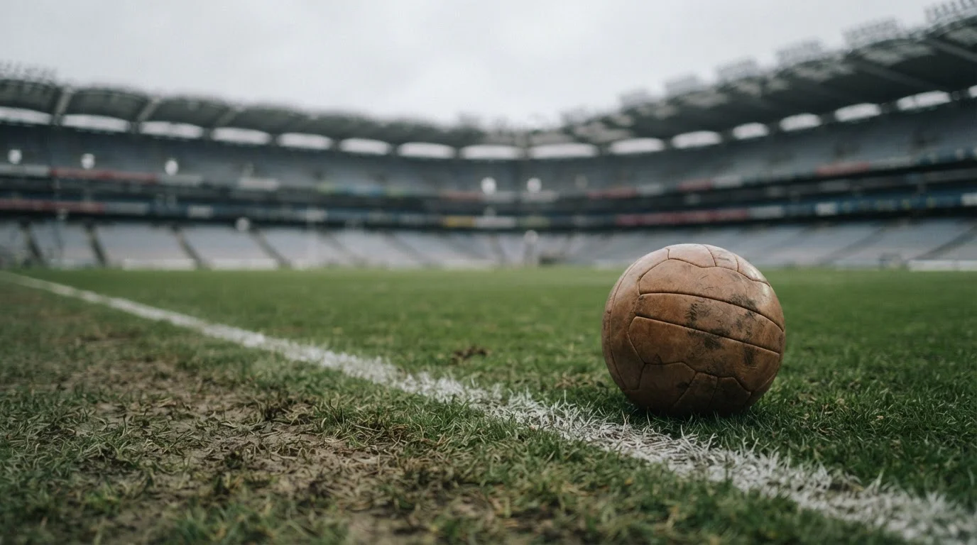 Balón de fútbol gastado sobre césped natural con luz suave de tarde