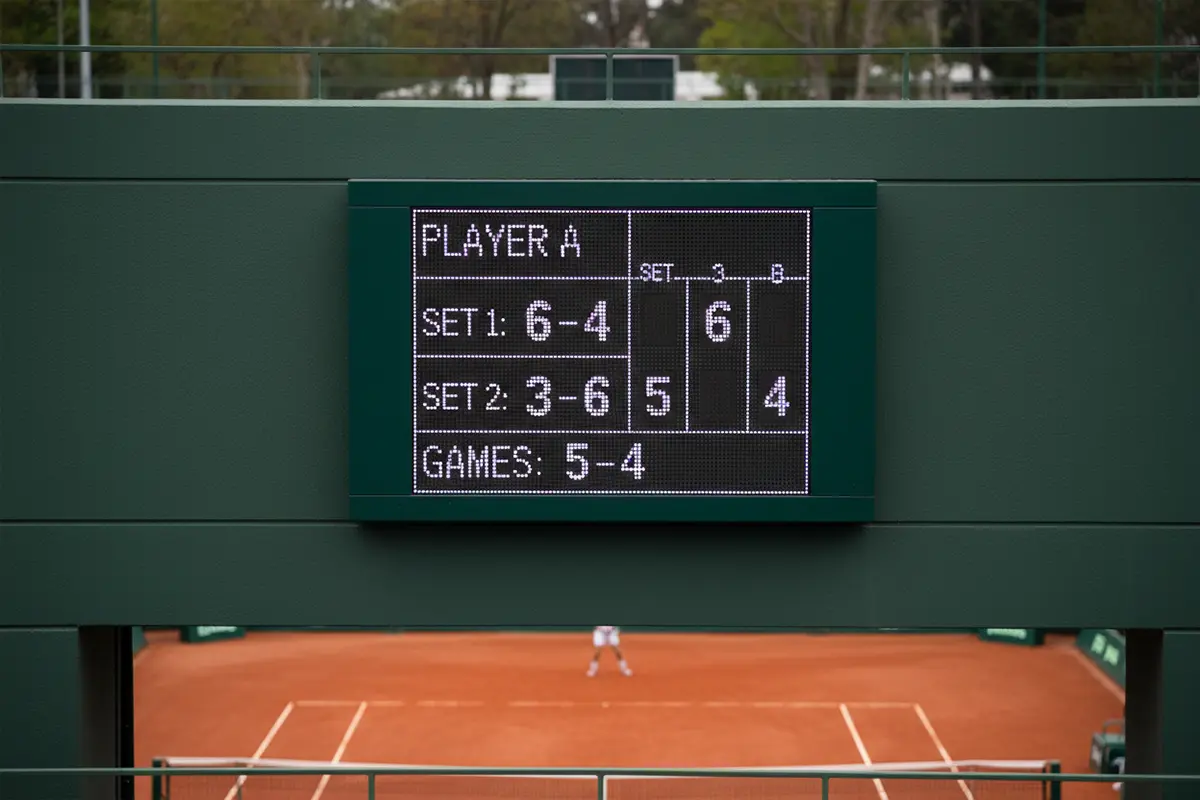 Marcador de partido de tenis mostrando sets y juegos en una pantalla electrónica junto a la pista